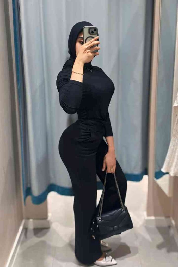 Dila, a beautiful Malay woman in a hijab, poses in black attire with a stylish handbag.