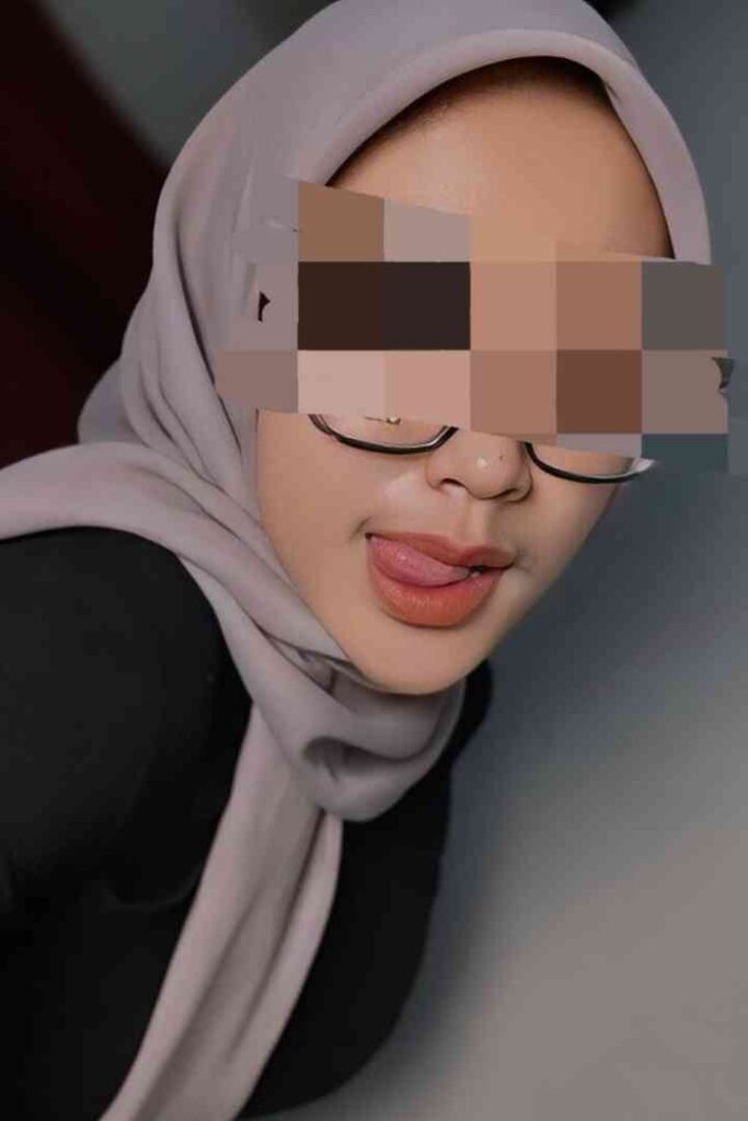 Dila, a 24-year-old Malay woman wearing a hijab and glasses, playfully sticking out her tongue.