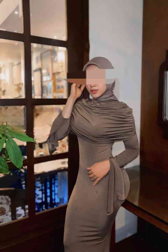 Dila, a stunning 24-year-old Malay woman in KL, wearing a stylish dress and hijab.