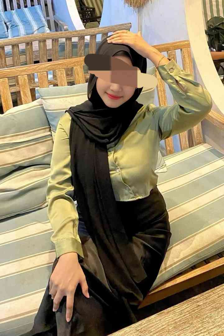 Woman in hijab and satin outfit sitting on a striped bench.